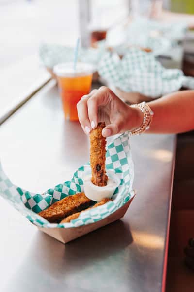 Hand dipping a crispy fried appetizer into sauce, showcasing popular coastal comfort food.