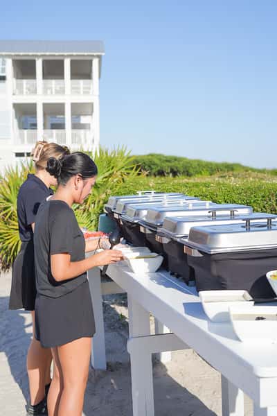 Restaurant staff preparing a buffet setup on the outdoor patio for a catered event overlooking the waterfront.