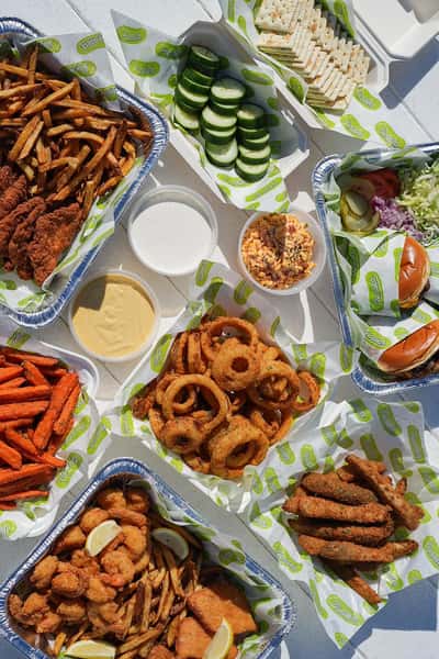 Outdoor seafood feast featuring fried shrimp, onion rings, sandwiches, sauces, and fresh sides at a coastal restaurant.
