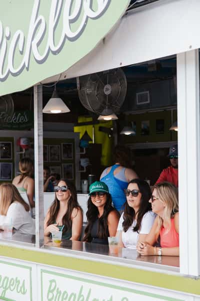 Friends smiling outside a beachfront restaurant entrance, enjoying a fun day by the shore.