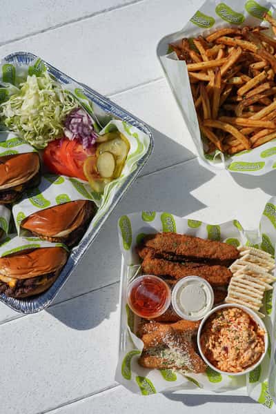 Catered meal featuring a gourmet burger, crispy fries, fresh vegetables, crackers, and dipping sauces for outdoor events.