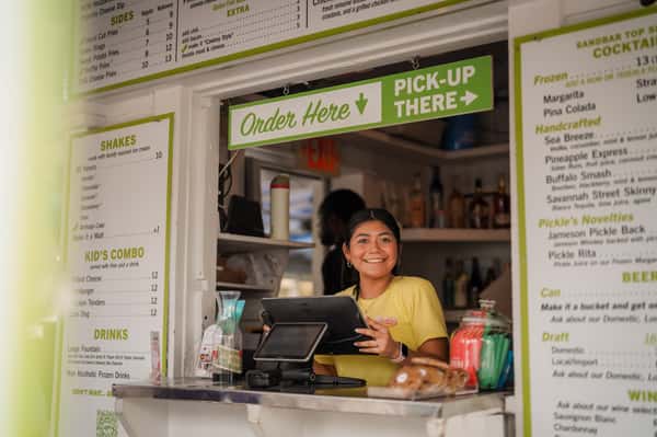 Friendly restaurant team member serving guests from a beachside takeout and pickup window.