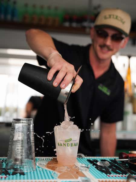 Sandbar bartender handcrafting a frozen cocktail behind the bar with fresh ingredients and expert preparation.