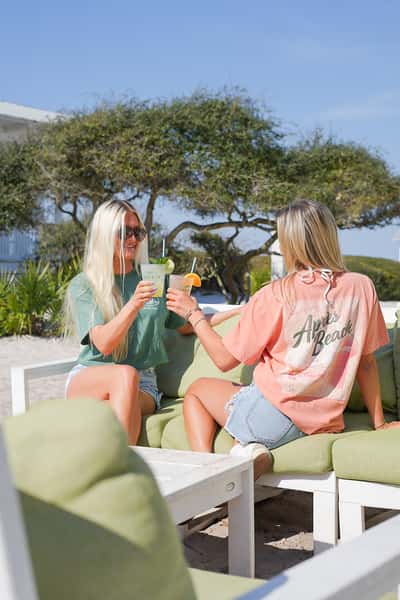 Guests enjoying drinks and conversation on an outdoor patio surrounded by palm trees, highlighting a vibrant beachside restaurant setting.