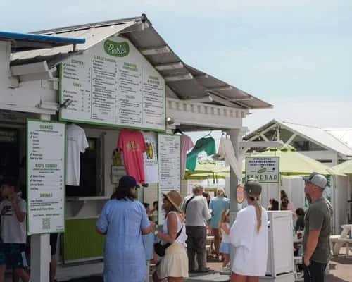 Customers ordering at a busy beachfront restaurant counter with outdoor seating and a lively coastal atmosphere.
