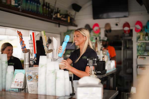 Smiling bartender preparing handcrafted frozen cocktails behind the bar at Sandbar, showcasing friendly service and a lively waterfront atmosphere.