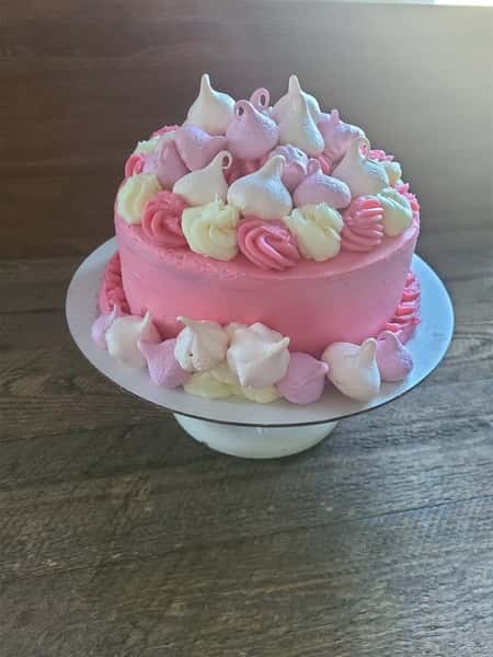 Circular cake with pink frosting and decorated with frosting swirls and meruinge