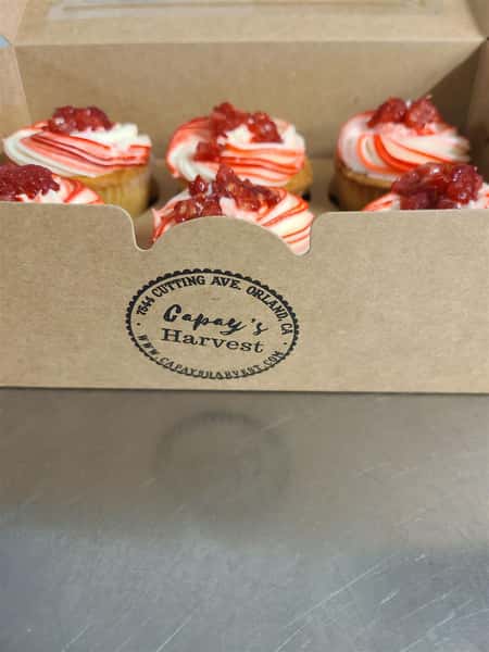 Box of a half dozen cupcakes with white and red streaked rfosting and topped with a berry compote