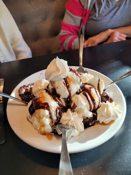 A plate of ice cream topped with whipped cream, chocolate syrup, caramel sauce, and multiple spoons ready to serve.