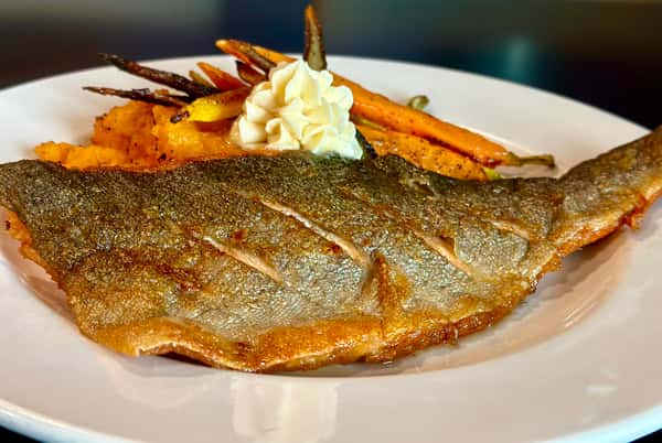 A plate of grilled fish served with mashed potatoes, roasted carrots, and a dollop of cream on top.