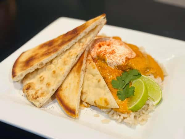 A plate of naan bread with rice, chicken curry, topped with sour cream, cilantro, lime wedges, and sprinkled with paprika.