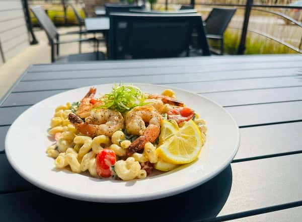 Shrimp pasta with creamy sauce, served with a slice of lemon and garnished with green onions. The dish is placed outdoors on a sunny day.