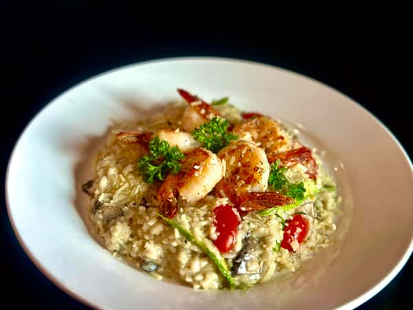 A plate of shrimp risotto with seasoned shrimp on top, garnished with parsley and accompanied by tomatoes and asparagus.