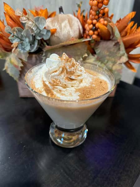 A creamy drink topped with whipped cream and cinnamon, placed near autumn-themed decor.