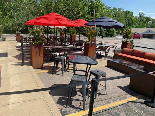 Outdoor restaurant patio with tables, bar seating, and red and black umbrellas creating a relaxed, open-air dining atmosphere.