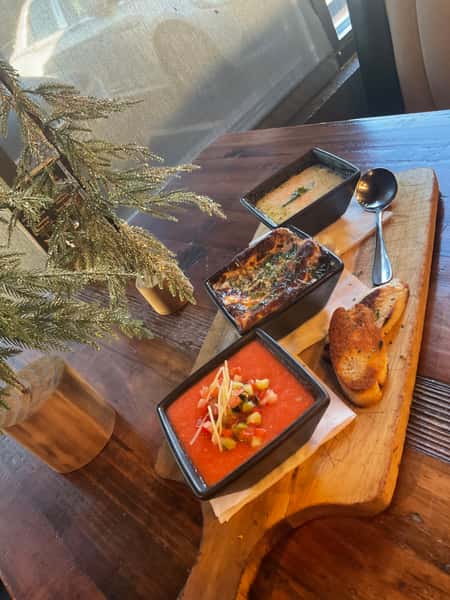 Trio of house-made soups served in black bowls with toasted bread on a wooden board, styled for a cozy restaurant dining experience.