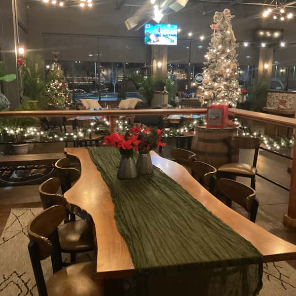 Festive restaurant dining area with a large communal table, holiday décor, string lights, and Christmas trees creating a cozy atmosphere.