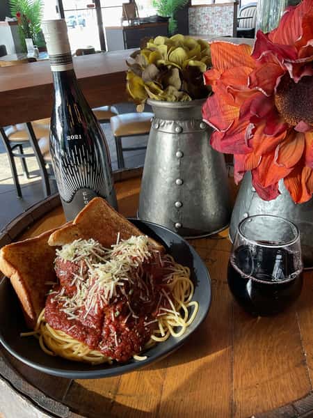 Spaghetti and meatballs topped with marinara sauce and grated cheese, served with toasted bread and red wine on a wooden table.