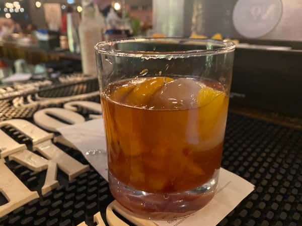 Old fashioned cocktail with orange peel and large ice cube, served at a craft cocktail bar with warm ambient lighting.
