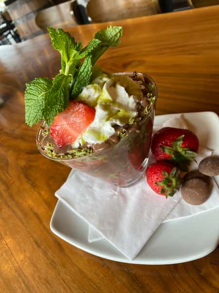 Layered chocolate dessert topped with whipped cream, fresh strawberries, mint leaves, and chocolate truffles, served on a white plate.