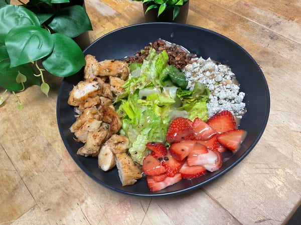 Grilled chicken salad bowl with romaine lettuce, strawberries, crumbled cheese, and vinaigrette, presented on a wooden table.