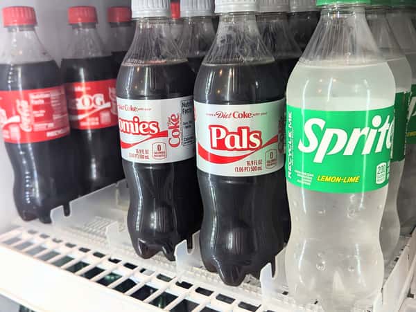 Assortment of Coca-Cola products and Sprite lemon-lime soda bottles in a fridge — refreshing mainstream soda options alongside specialty drinks.