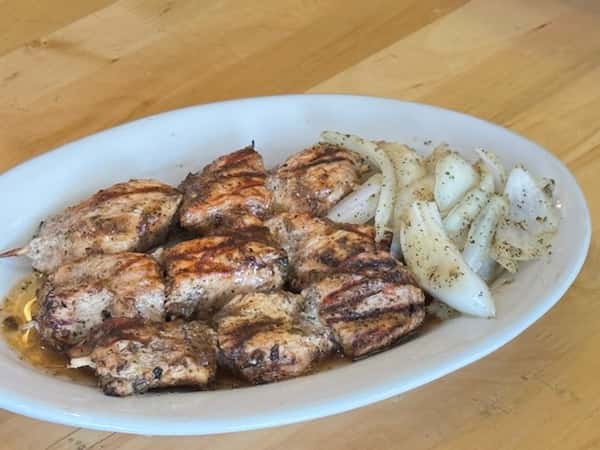 Juicy grilled chicken kebabs served with seasoned sautéed onions on a white plate — a popular protein-rich entrée in African and Caribbean cuisines.