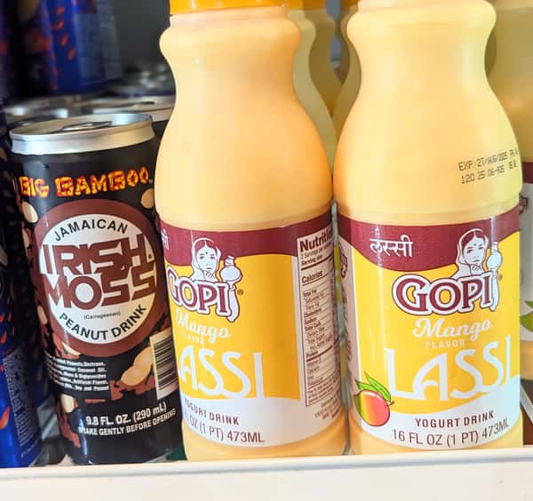 Jamaican Irish Moss peanut drink and Gopi mango lassi yogurt beverages lined up in a fridge — a fusion of Caribbean and South Asian traditional drinks.