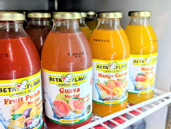 Variety of Beta Flava Jamaican fruit nectars, including guava, fruit punch, and mango carrot, displayed in glass bottles inside a refrigerated cooler.