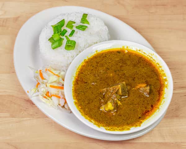 Plate of white rice garnished with chopped green onions, served alongside a bowl of rich, dark green Nigerian ogbono soup with chunks of meat, accompanied by a side of tangy cabbage slaw.