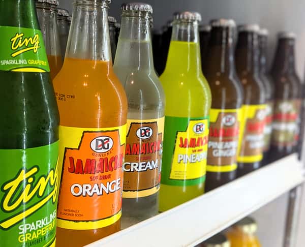 Variety of DG Genuine Jamaican soft drinks including orange, cream, and pineapple flavors, along with Ting sparkling grapefruit soda — a colorful selection of traditional Caribbean beverages.