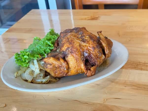 Whole deep-fried chicken seasoned with West African spices, served with sautéed onions and fresh romaine lettuce on a white plate.