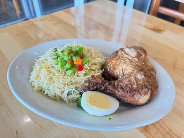 Spiced fried chicken leg served with seasoned vermicelli noodles, bell peppers, and a boiled egg — a hearty West African-inspired dish.