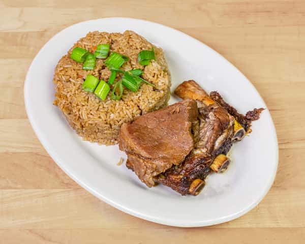 Plate of Nigerian jollof rice garnished with chopped green onions, served with tender beef and smoky grilled ribs, offering a hearty and flavorful West African meal.