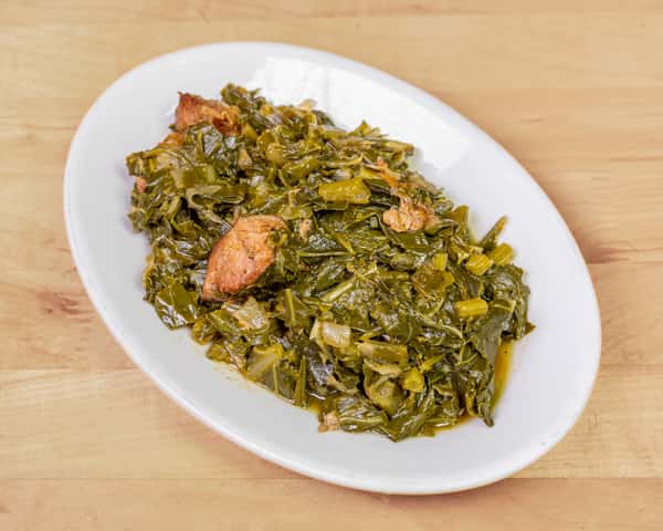 Slow-cooked collard greens with chunks of smoked meat served on a white plate — a savory Southern and African soul food staple.
