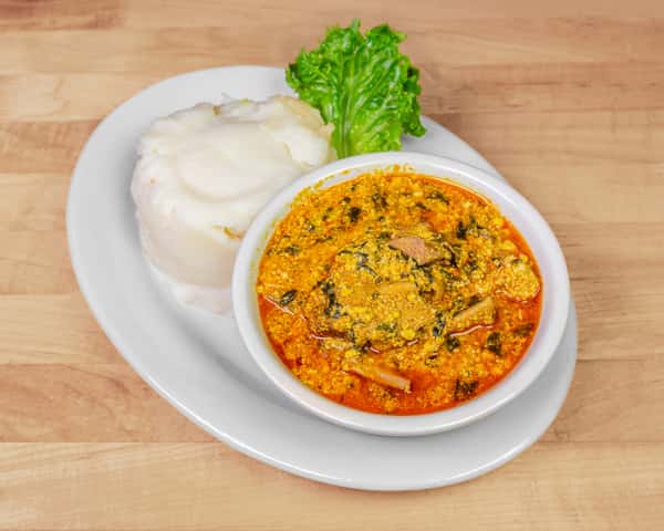 Bowl of Nigerian egusi soup made with melon seeds, leafy greens, and assorted meats, paired with a serving of smooth white fufu and garnished with fresh lettuce.