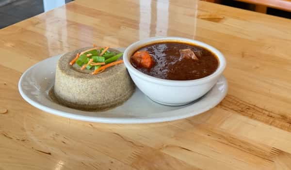 Traditional West African plate featuring a molded serving of millet or acha, garnished with shredded carrots and green onions, paired with a bowl of rich beef and vegetable stew.