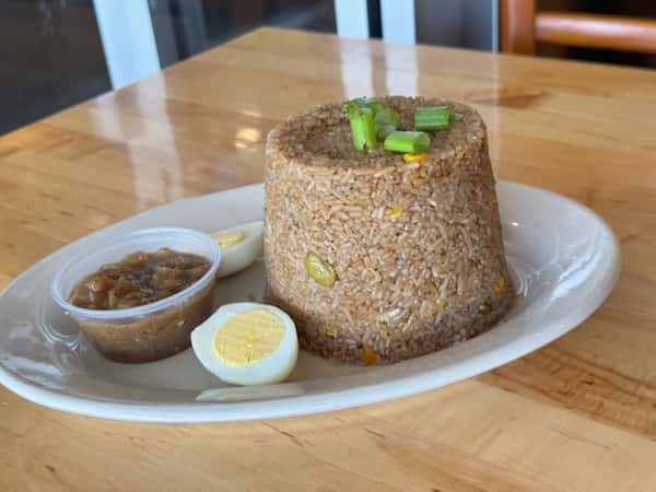 Molded serving of spiced West African-style rice garnished with green onions, accompanied by boiled egg halves and a savory onion-based sauce — a comforting traditional rice dish.