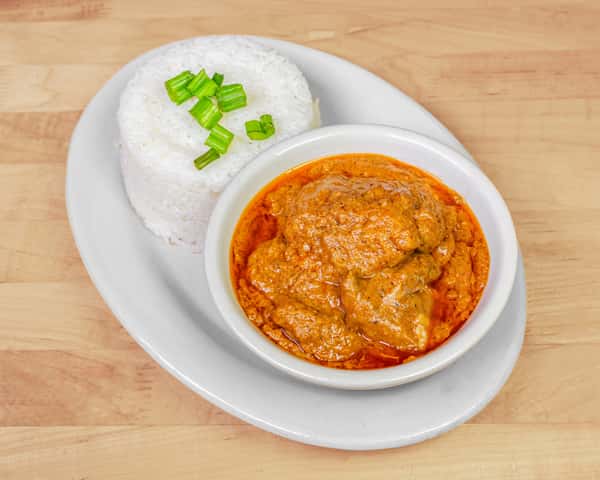 Bowl of creamy Nigerian groundnut (peanut) stew with chicken, paired with a molded serving of steamed white rice topped with chopped green onions.