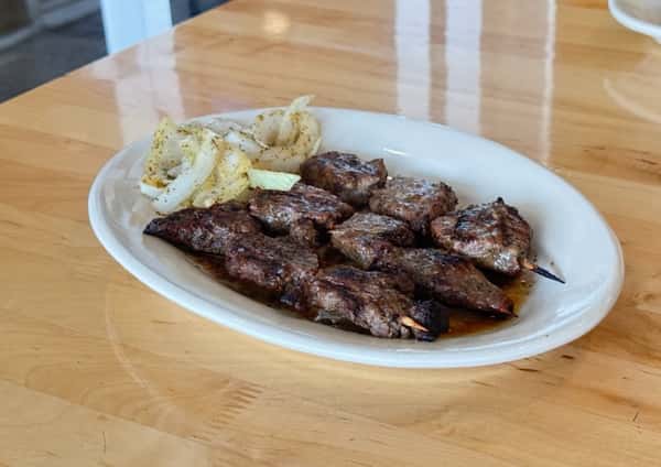 Juicy grilled beef skewers served with sautéed onions on a white plate — a flavorful African or Caribbean grilled meat dish perfect for meat lovers.