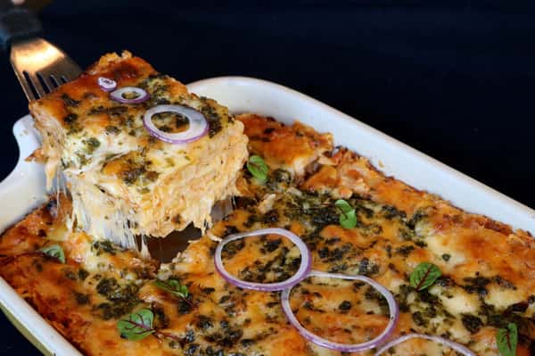 Southern-style seafood casserole topped with melted cheese, herbs, and red onion, baked to perfection and served fresh at Hugo's restaurant.