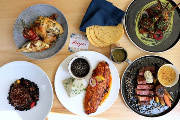 Assorted Southern-inspired entrées and appetizers at Hugo's restaurant, featuring grilled seafood, fresh sides, cornbread, and house-made specialties.