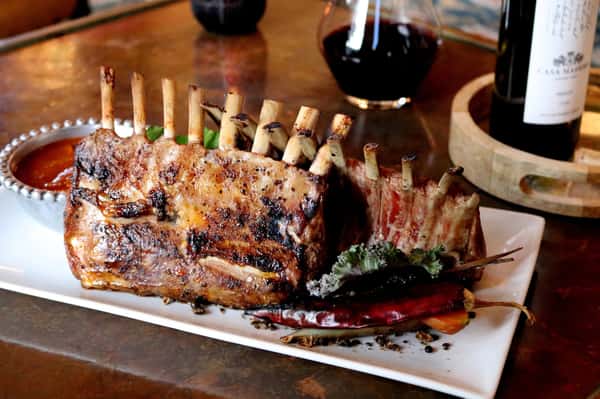 Grilled rack of lamb expertly prepared and plated with seasonal accompaniments at Hugo's restaurant.