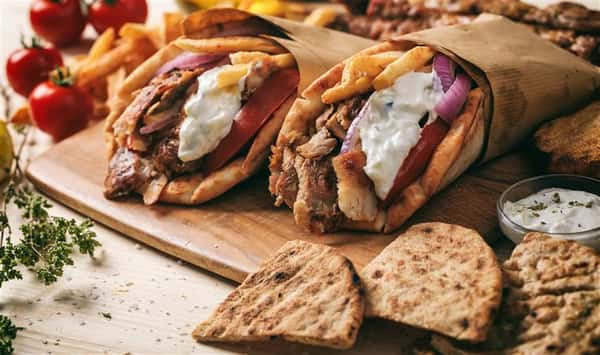 greek gyros on a wooden board with sliced pitas on the side