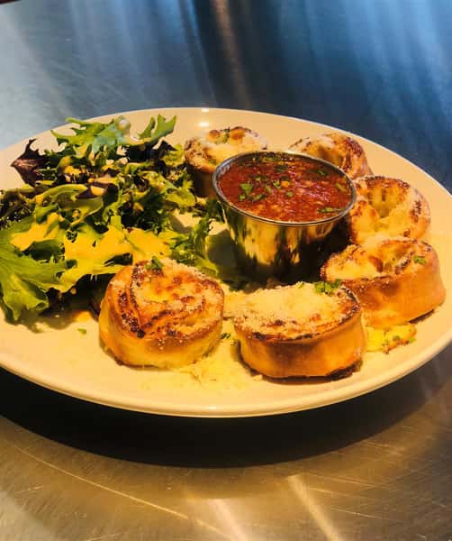 Stromboli topped with Parmesan cheese with a side of Marinara sauce and greens on the side on a plate