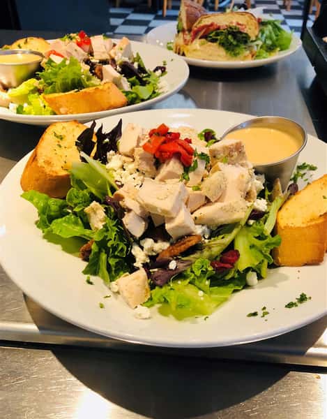 Candied pecans, sundried cranberries, feta cheese, raspberry Dijon honey mustard vinaigrette on a plate with other salads in the background
