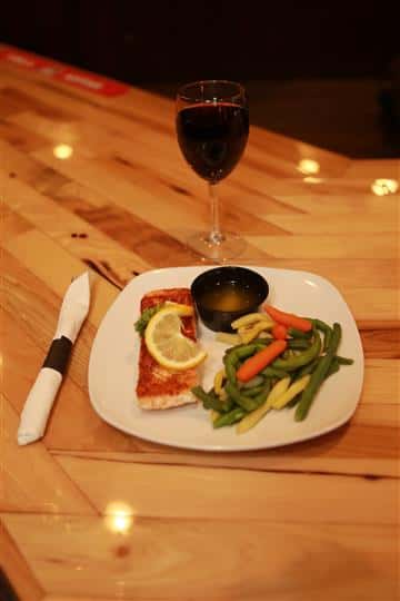 Grilled Salmon with lemon on top and a side of mixed vegetables and butter. Glass of red wine is on the side.