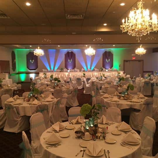 Indoor view of banquet room set for event with white linens and blue bows tied around the chairs.