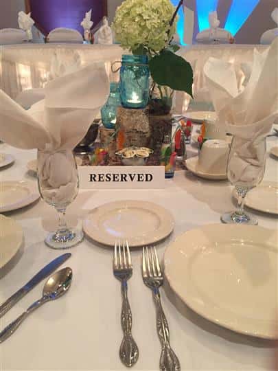 Close up of table setting reserved with white linens and plates and a blue mason jar with a plant as the centerpiece.