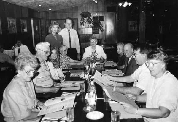 Black and white image of 11 people around a table looking at menus.